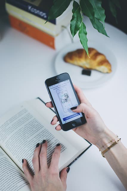A hand holding a phone showing an app sign-in screen above an open book